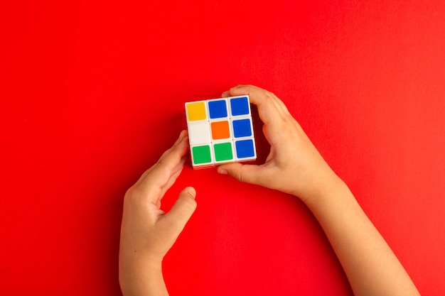 Free photo top view little kid playing with rubics cube on red desk