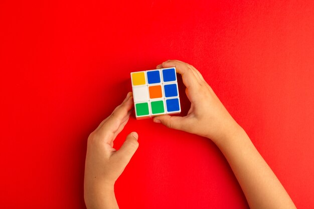 Вид сверху маленький ребенок играет с кубиком рубика на красном столе