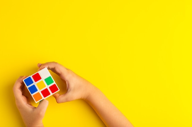 Top view little kid playing with rubics cube on the yellow surface