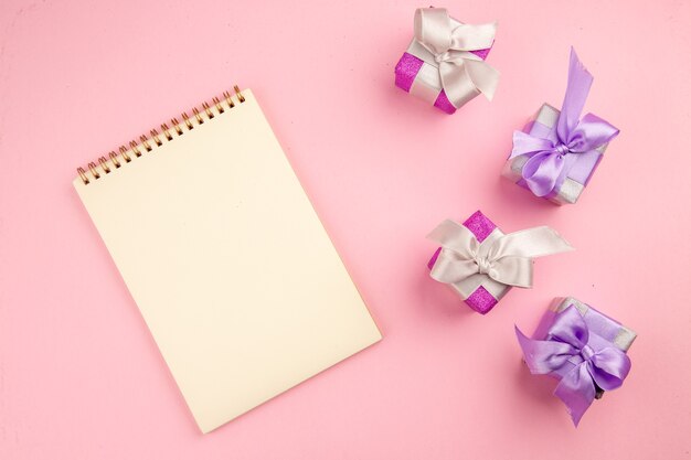 Top view of little presents with notepad on a pink surface