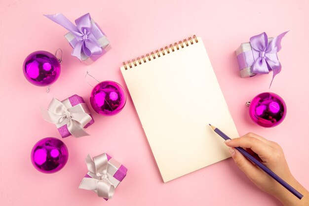 ピンクの表面にクリスマスツリーのおもちゃとメモ帳と小さなプレゼントの上面図