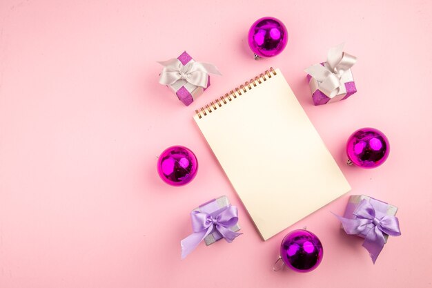 Top view of little presents with xmas tree toys and notepad on pink surface