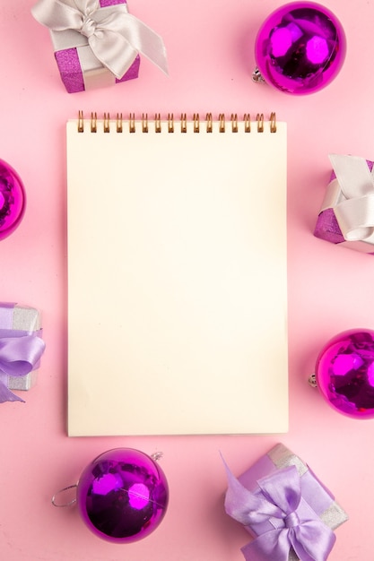 Top view of little presents with xmas tree toys and notepad on pink surface