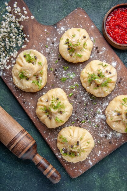 Вид сверху маленькие сырые пельмени с мясом и томатным соусом на темно-синей поверхности мясное тесто блюдо торт ужин приготовление еды