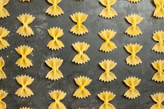 Top view little raw pasta spread all over dark-grey background