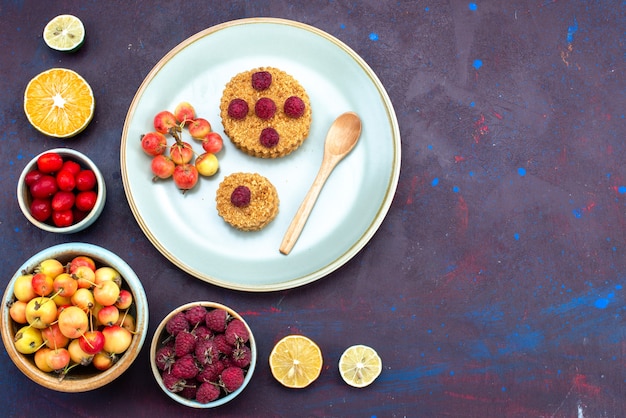 Foto gratuita vista dall'alto della piccola torta rotonda con lamponi freschi all'interno del piatto con frutta fresca sulla superficie scura