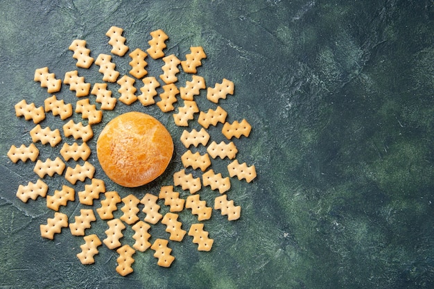 Top view of little salted crackers with little cake on dark surface