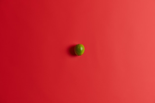 Top view of little sour green lime lying on red vibrant surface, contains much vitamins. Fresh juicy citrus fruit for nutrition. Ingredient for making mojito or lemonade. Healthy food concept.