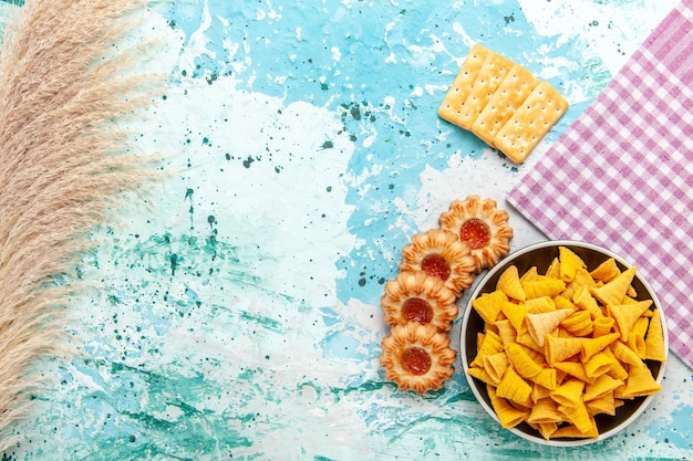Вид сверху маленькие острые чипсы внутри тарелки с крекерами и печеньем на светло-синем фоне чипсы закуска цвета хрустящие калории