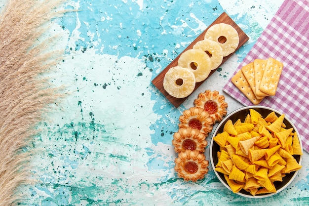 Top view little spicy chips with crackers dried pineapple rings and cookies on light-blue background chips snack color crisp calorie