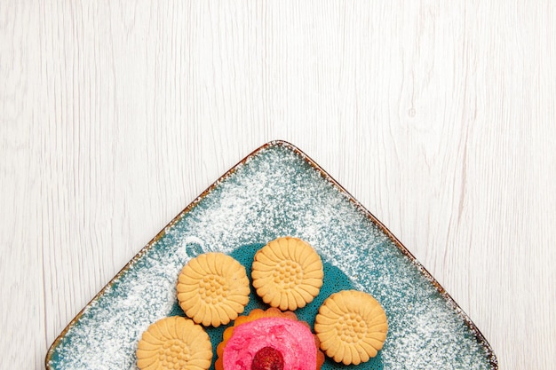 Top view of little sweet cookies with fruit cake inside plate on white table