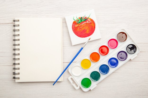 흰색 테이블에 다채로운 페인트가 있는 상위 뷰 작은 토마토 그리기