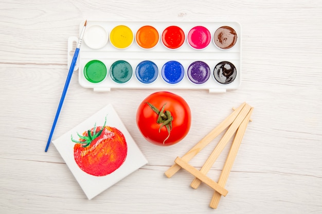 Top view little tomato drawing with colorful paints on white table