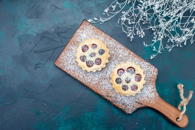 Top view little yummy cake with sugar powder and cherries on the dark-blue background fruit cake biscuit sweet photo color