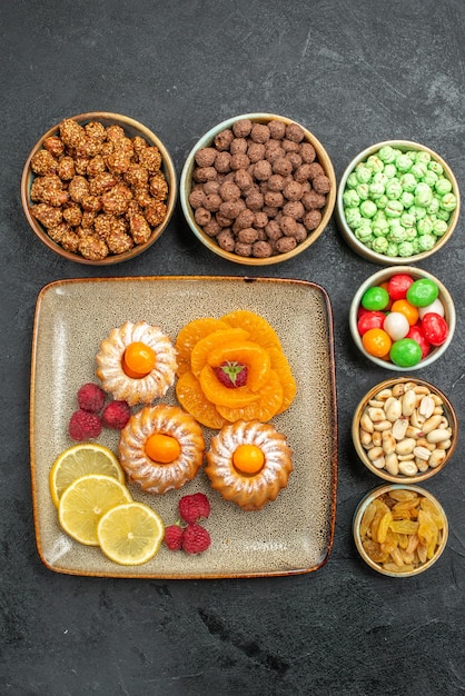 Foto gratuita vista dall'alto di piccole deliziose torte con caramelle, frutta e noci su grigio