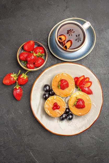 Free photo top view little yummy pancakes with fruits and cup of tea on the grey surface pie cake fruit