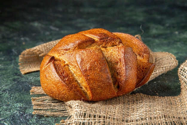 Top view of a loaf of dietary black bread on brown towel on dark colors surface with free space