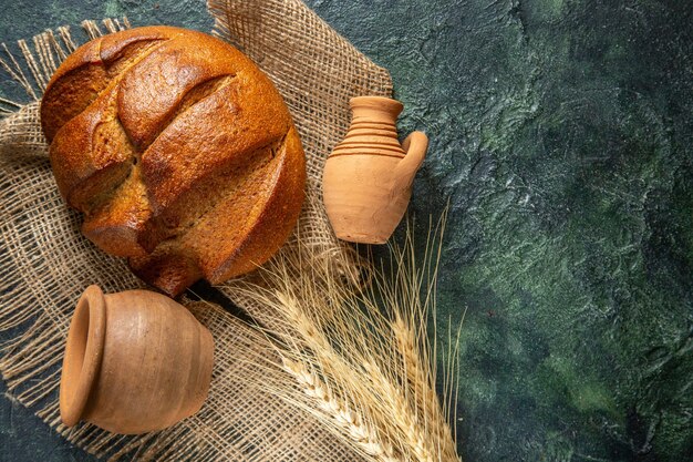 暗い色の背景の右側に茶色のタオルと陶器の食餌療法の黒いパンのパンの上面図