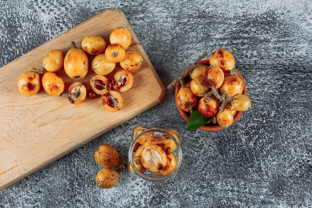 Free photo top view loquats in jar, bowl and cutting board on gray textured background. horizontal