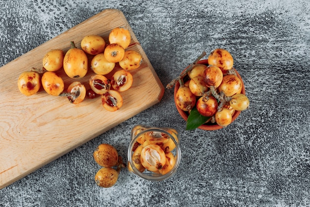 Top view loquats in jar, bowl and cutting board on gray textured background. horizontal