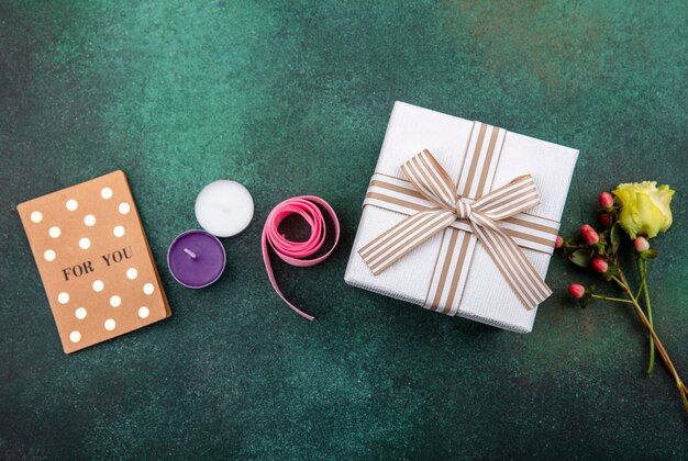 Top view of lovely and tender flower with gift box on green surface