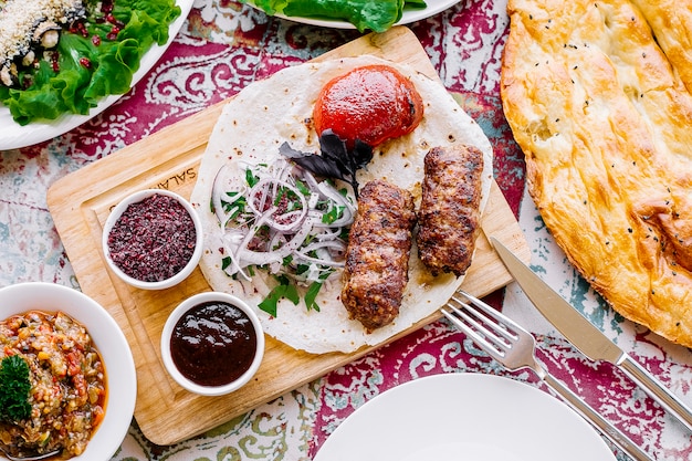 Foto gratuita vista dall'alto lula kebab sul pane pita con cipolle pomodoro e salse sul tavolo