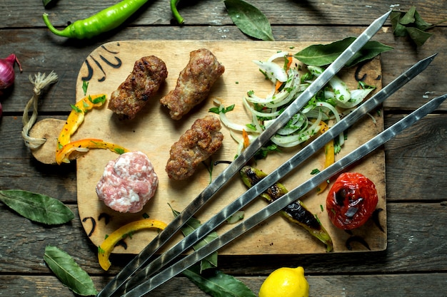Top view of lula kebab with onion herbs grilled vegetables and skewers on a wooden board
