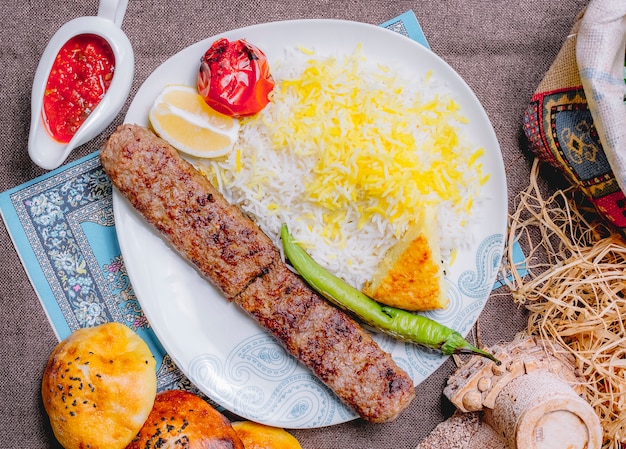 Free photo top view lula kebab with rice tomato and green pepper grilled with a slice of lemon and sauce