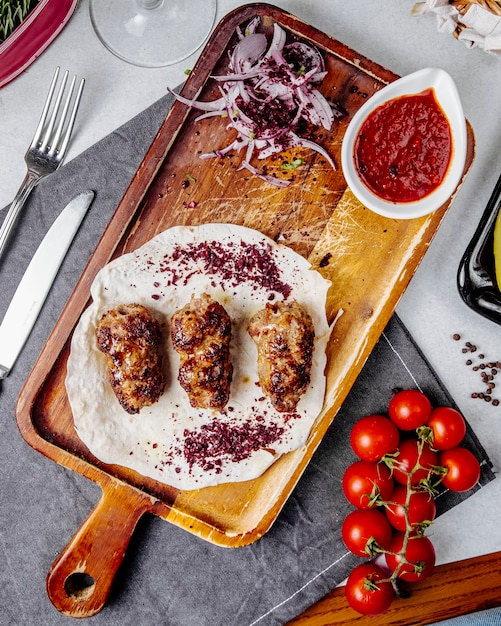 Top view of lule kebab with red onions on a wooden board