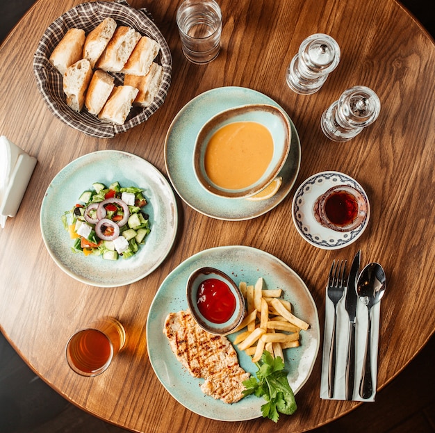 グリルチキン料理のレンズ豆のスープのパンとギリシャ風サラダのランチセットアップのトップビュー