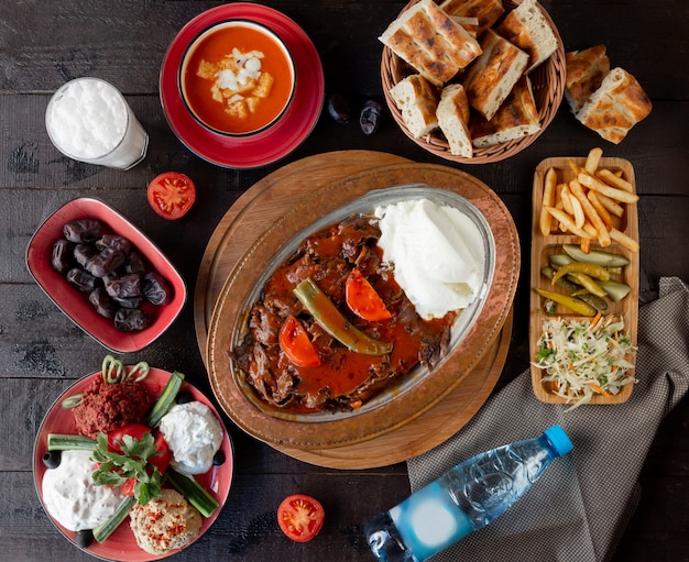 Top view of lunch setup with iskender kebab, tomato soup, pickles, turkish meze