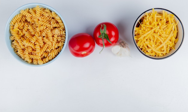 Top view of macaronis as rotini and tagliatelle with tomatoes and garlic on white with copy space
