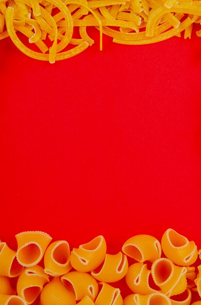 Вид сверху макарон в виде тальятелле и трубчатой на красной поверхности с копией пространства