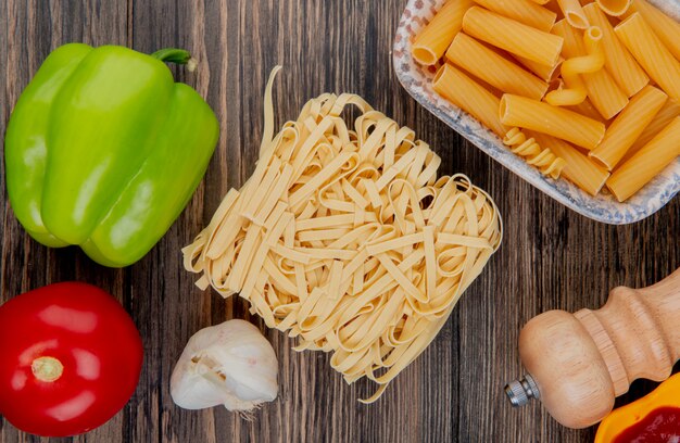 Top view of macaronis as tagliatelle ziti with pepper garlic tomato salt on wooden surface