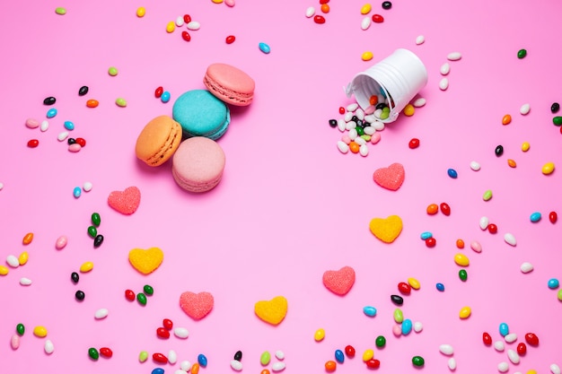 A top view macarons and marmelade colorful french cakes along with multicolored candies on the pink background sweet candy