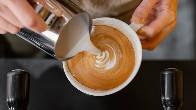 Top view of male barista pouring milk in coffee cups
