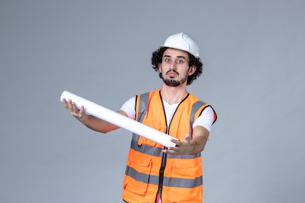 Vista dall'alto del costruttore maschio in giubbotto di avvertimento che indossa il casco di sicurezza e dà il vuoto sulla parete grigia dell'onda