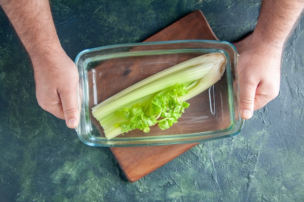 Top view male cook holding plate with celery on dark table salad diet meal color photo food health