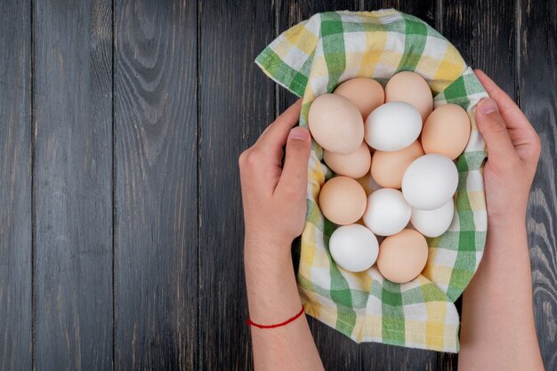 Top view of male hands holding multiple fresh chicken eggs on checked tablecloth on a wooden background