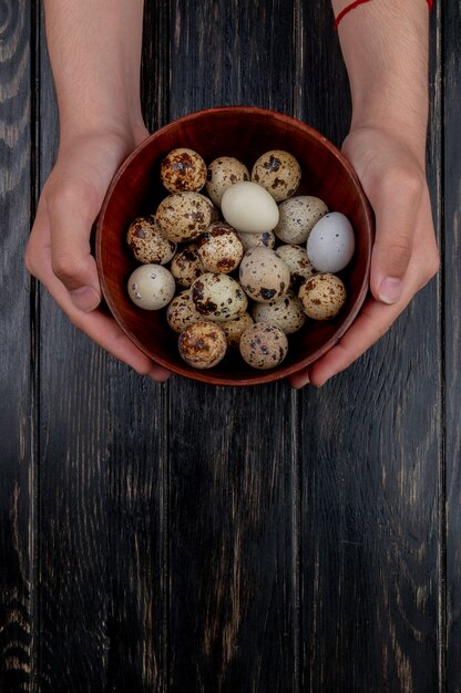 Top view of male hands holding quail eggs on a wooden bowl on a wooden background with copy space