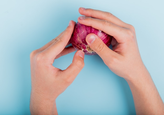 Free photo top view of male hands holding red onion on blue table