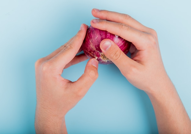 Top view of male hands holding red onion on blue table