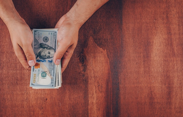 Free photo top view man holding hundred dollar bills on wooden