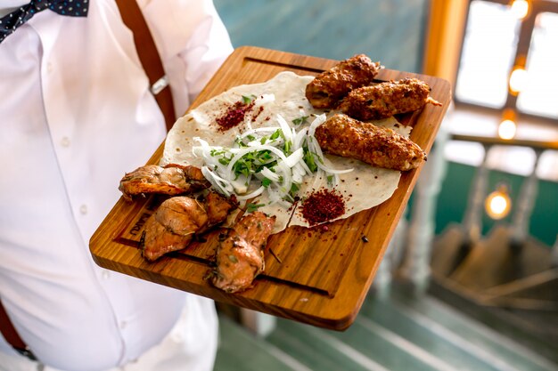 Top view a man holds a tray with lula and tike kebab on a pita with onions and herbs