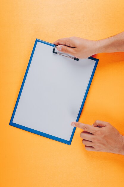 Top view man pointing to clipboard while holding it on orange