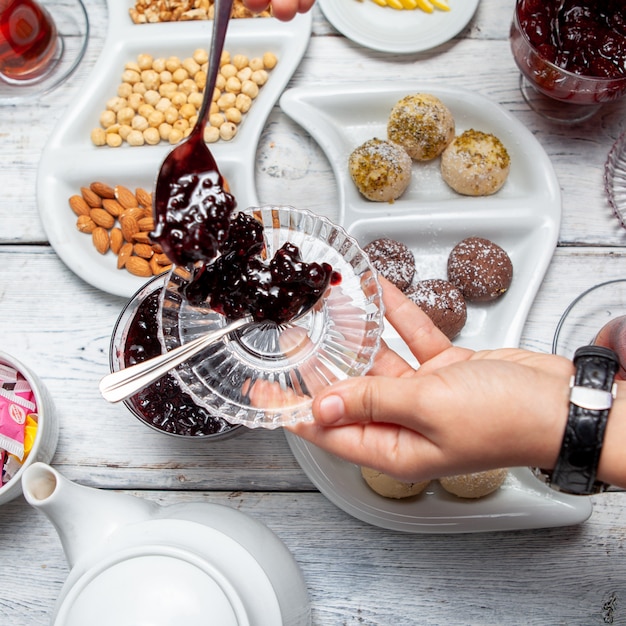 Top view man serving delicious fruit jam with tea, nuts on white wooden background.