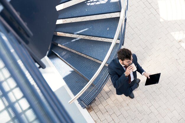 Top view man with tablet drinking coffee near stairs