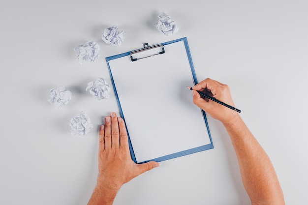 Top view man writing on clipboard with crumpled papers on white