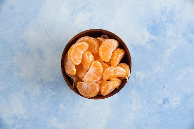 Вид сверху ломтиков мандарина в деревянной миске на синей поверхности