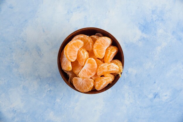 Top view of Mandarin slices in wooden bowl on blue surface